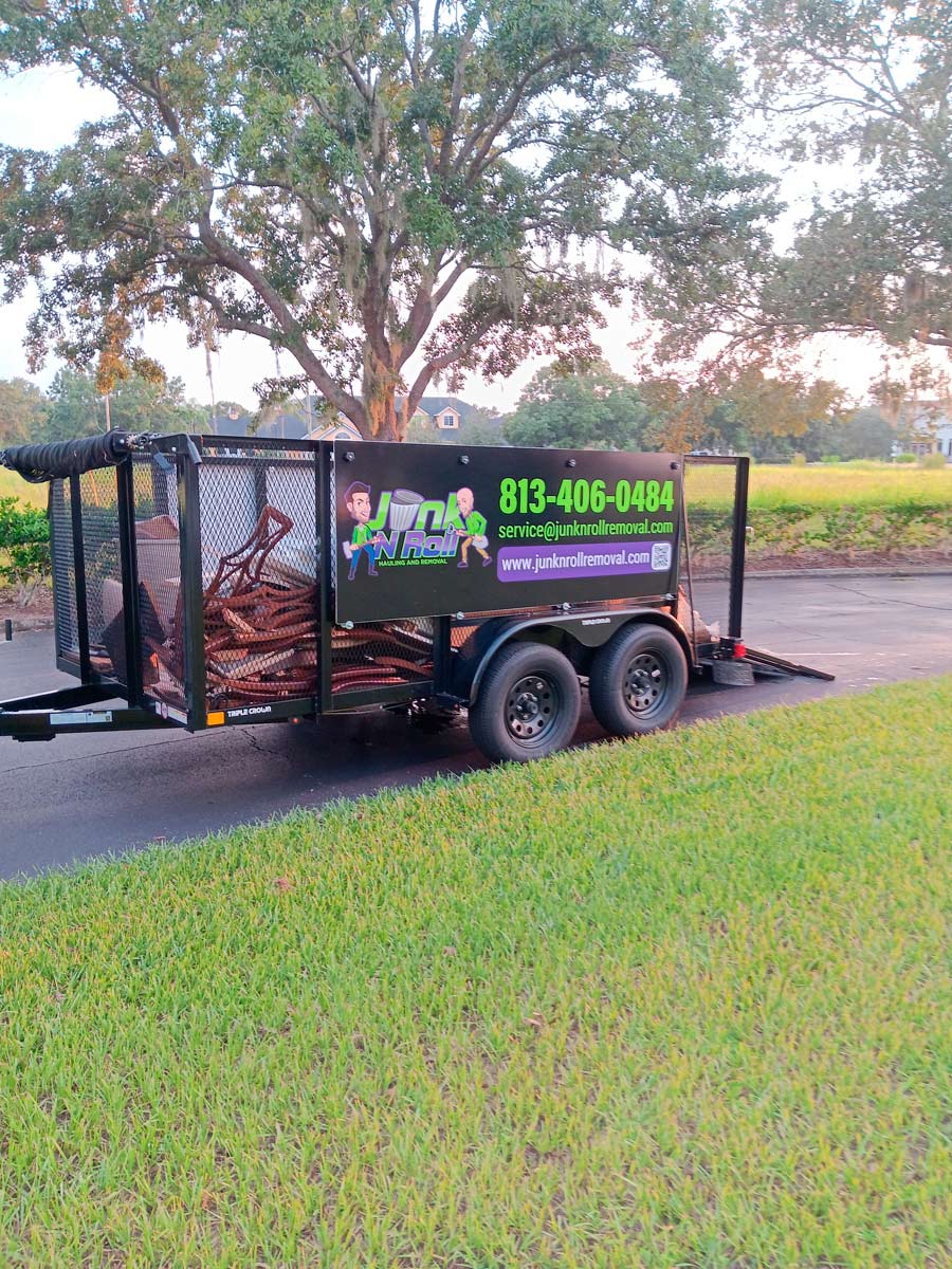 Out With the Old, In with the New: Start Spring 2025 Fresh with a Junk-Free Home 8 A trailer labeled with Junk Roll branding, featuring a phone number and contact info, is parked on a road beside a grassy area. It carries assorted metal debris. A large tree and houses are visible in the background.