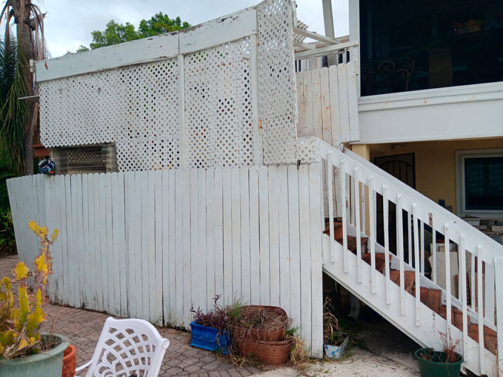 Bradenton Outdoor Staircase Demolition 1 A weathered white wooden structure with lattice panels and stairs, surrounded by potted plants, in a residential outdoor area.