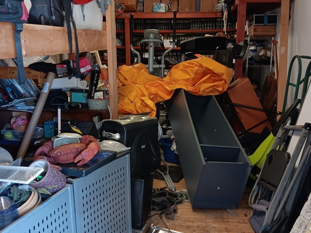 Garage Cleanout Hacks: Get It Done Fast & Efficiently 2 A cluttered garage filled with disorganized furniture, tools, and a large orange tarp, creating a chaotic environment.