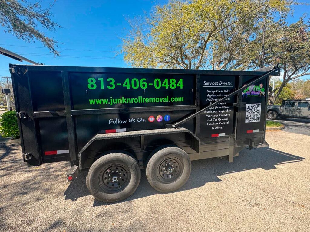 House Cleanout in Riverview 1 A black junk removal trailer with green lettering, showcasing services offered and contact information, parked under a blue sky.