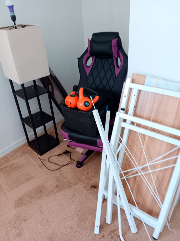House Cleanout in Riverview 9 A corner of a room featuring a gaming chair, a lamp, a small shelf, and disassembled furniture parts on a carpeted floor.