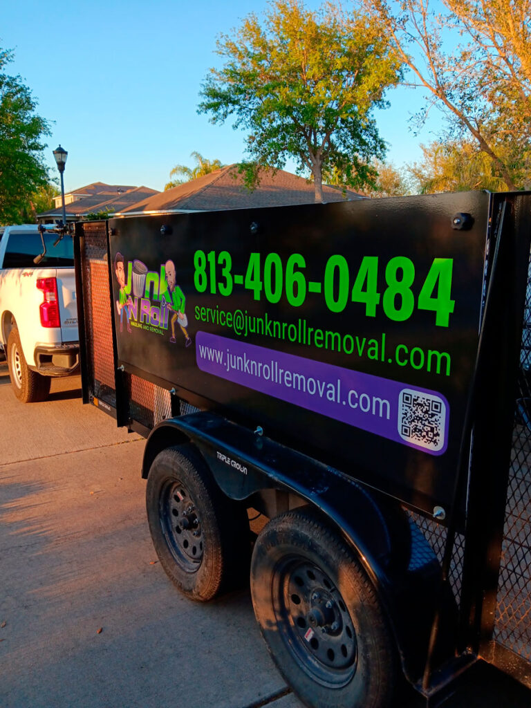 House Cleanout in Riverview 4 A trailer with a vibrant "Junk N Roll" advertisement features contact info and a QR code, parked by homes under a clear blue sky.