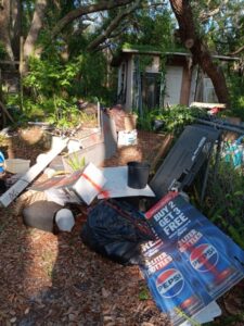 A cluttered backyard with a small shed and an old chain-link fence partially blocked by junk and debris.