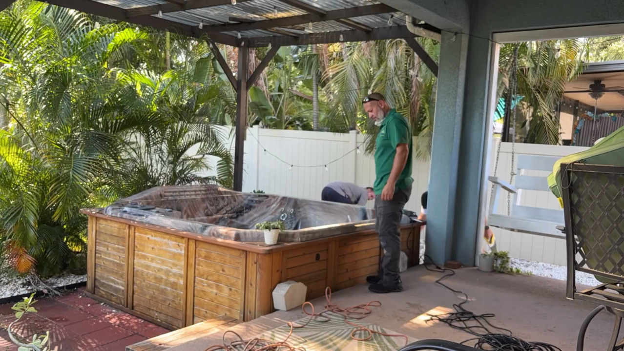 Workers are dismantling an old wooden hot tub on a patio.