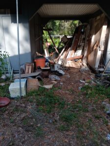 An unkempt yard with an old shed and various piles of junk and debris scattered around.