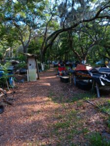 A messy, cluttered yard filled with various junk items, including an old grill, plastic bins, and discarded household items.