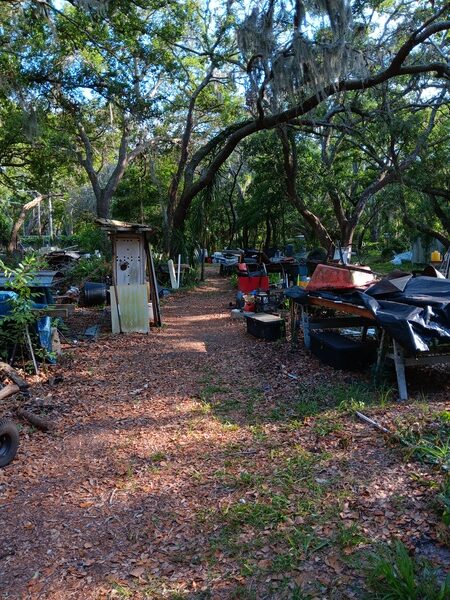 A messy, cluttered yard filled with various junk items, including an old grill, plastic bins, and discarded household items.