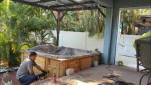 Two workers are in the process of dismantling a wooden hot tub on a patio.