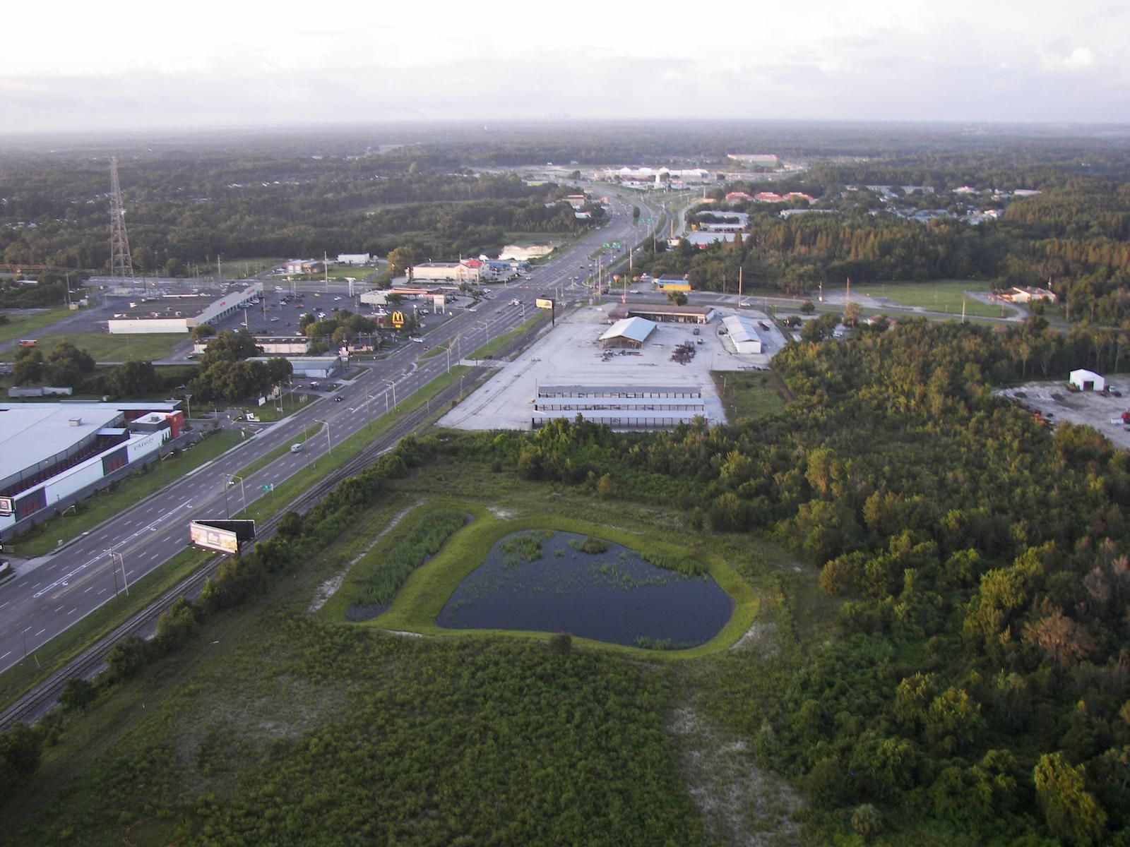Aerial view showcasing a mix of commercial buildings, a pond, and greenery under a cloudy sky.